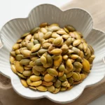 Perfect Roasted Pumpkin Seeds: Crispy & Flavorful Guide 4 A white ceramic bowl filled with perfectly roasted pumpkin seeds, glowing with a golden-brown hue.