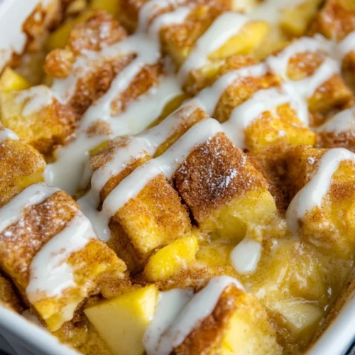 apple cinnamon french toast casserole in a white baking dish topped with glaze and grated apple