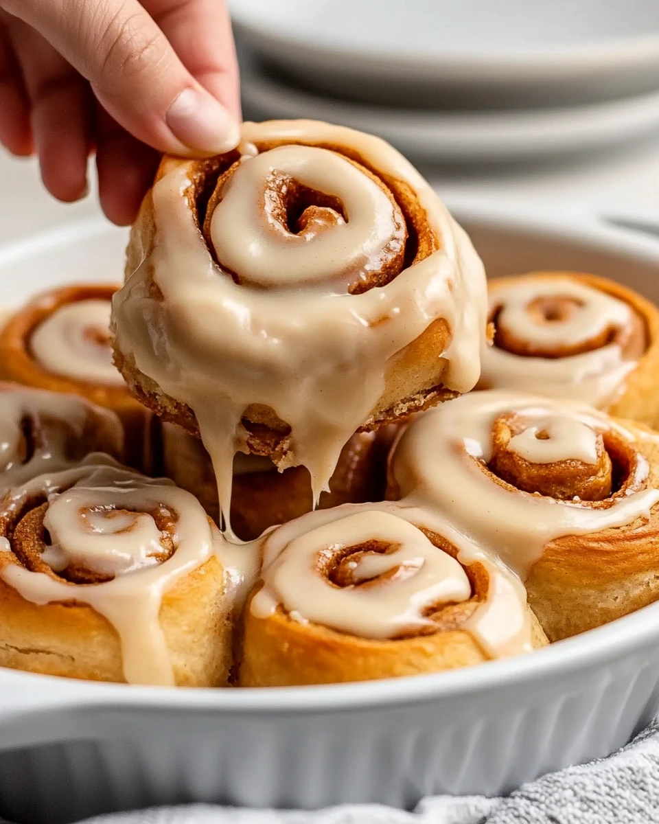Close-up of glazed gluten free vegan gingerbread cinnamon rolls, one being lifted from a pan.