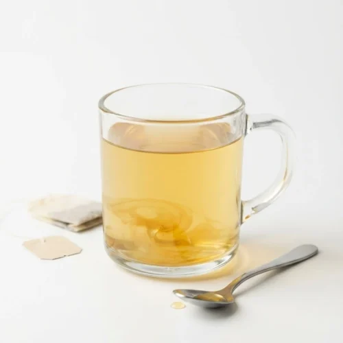 Clear glass mug of warm herbal tea sweetened with Canaan honey on a white background.