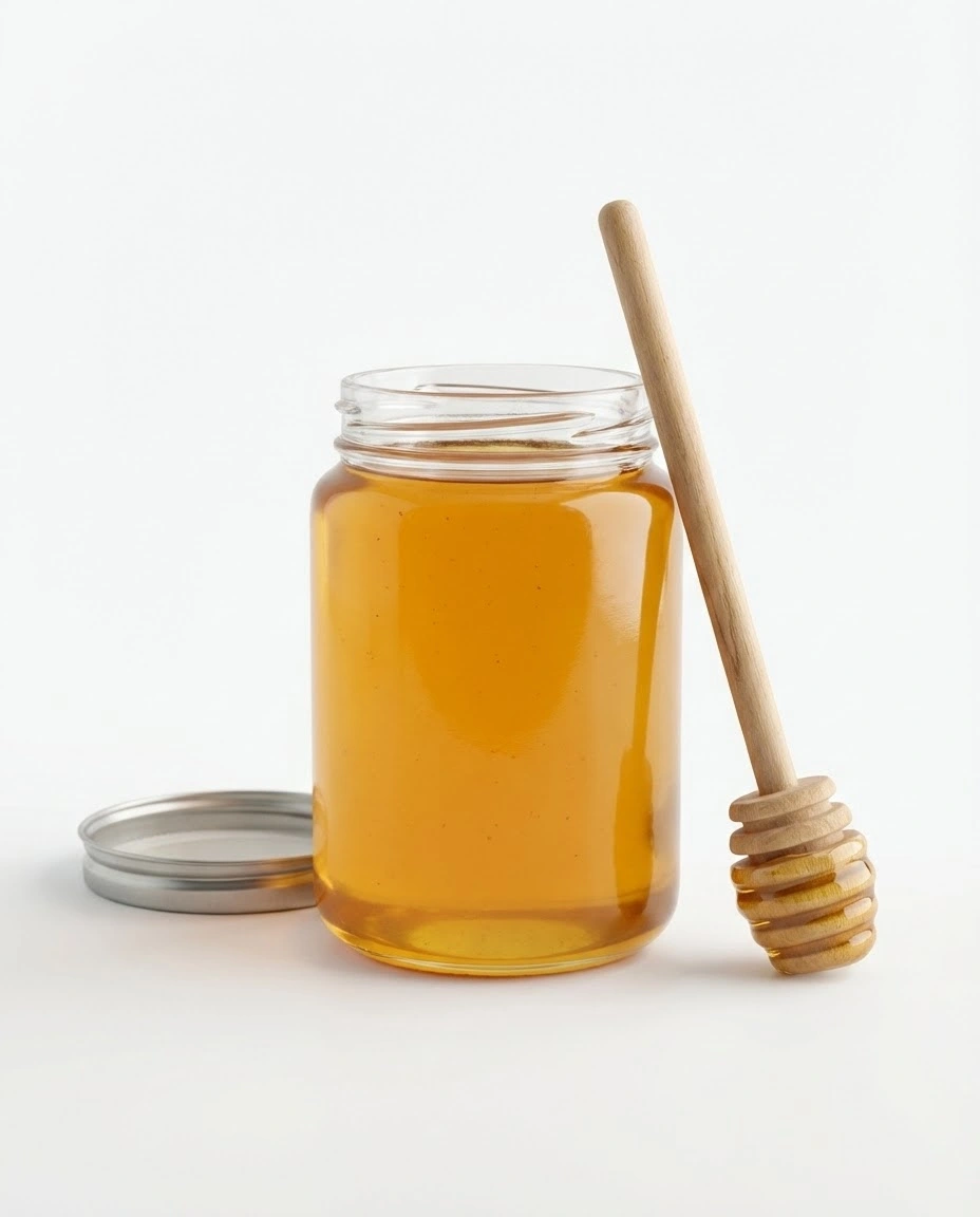 Plain glass jar of golden honey with a wooden dipper on a white background.