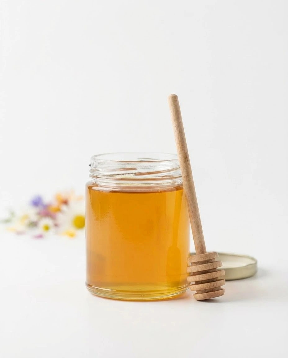 Clear jar of golden canaan honey with a clean wooden dipper on a white background.
