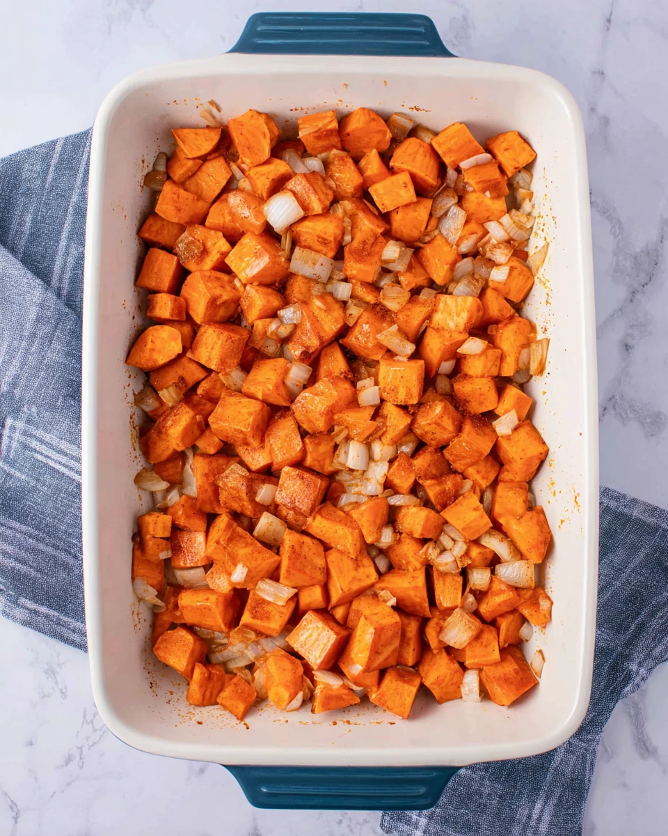 Top-down view of diced sweet potatoes and onions in baking dish for turkey sweet potato bake