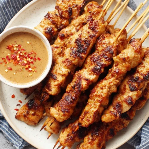 Chili garlic chicken satay skewers with creamy dipping sauce on a white plate