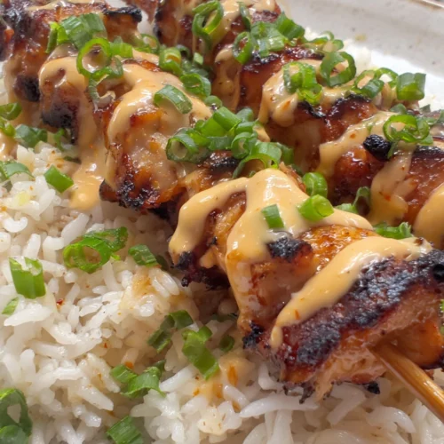 Chili lime chicken skewers over rice with creamy sauce and green onions
