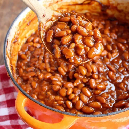 Old fashioned baked beans in a Dutch oven with a spoon, rich sauce and bacon bits