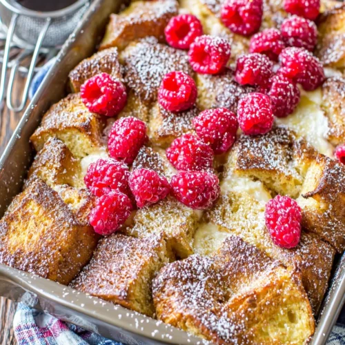 Raspberry cream cheese French toast bake topped with fresh berries and powdered sugar