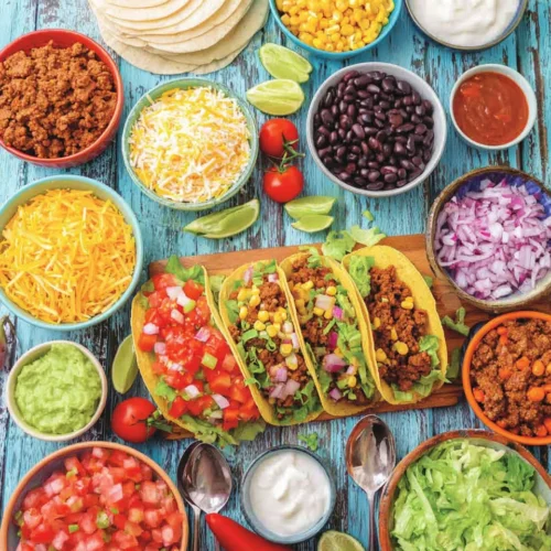 Delicious Taco Bar: An Easy, Interactive Meal 1 Colorful taco bar with tortillas, meats, cheeses, salsas, and fresh toppings on a blue wooden table.