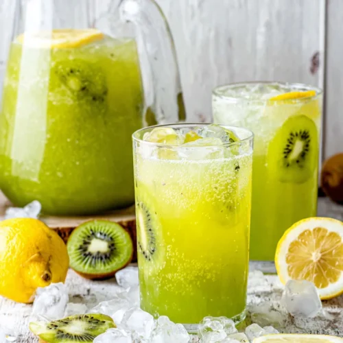 Bright green agua de kiwi in a pitcher and glasses with lemon slices and ice