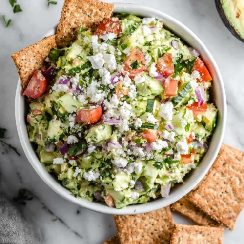 Avocado feta dip with tomatoes, herbs, and crackers in a white bowl