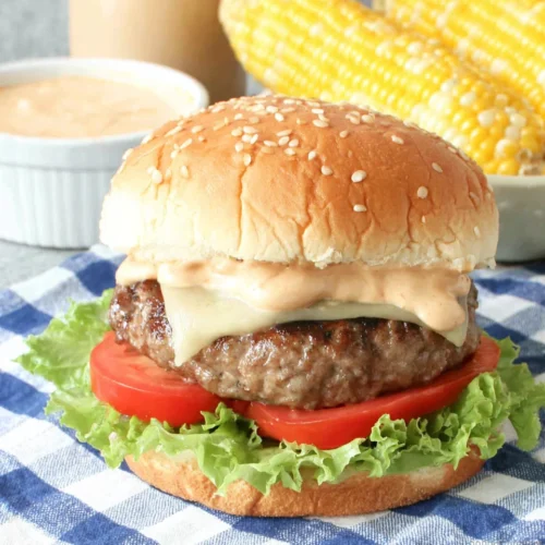 Juicy BBQ burger with cheese, lettuce, tomato, and sauce on a sesame bun, served with corn on the cob