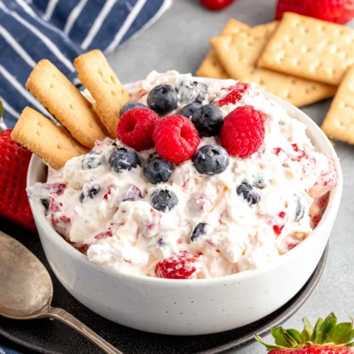 Berry cheesecake fluff in a white bowl topped with fresh berries and graham crackers