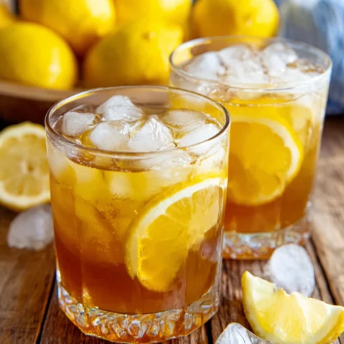 Two glasses of brown sugar lemonade with ice and lemon slices, fresh lemons in background