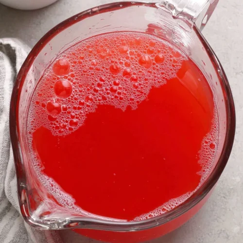 Canning watermelon lemonade concentrate in a glass pitcher with frothy bubbles.