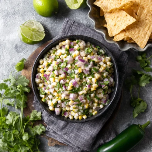 Chipotle corn salsa in a black bowl with tortilla chips and fresh ingredients