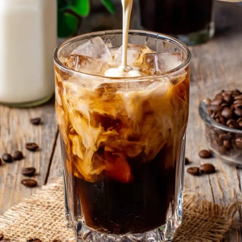 Cold Brew Coffee Recipes: Refreshing and Easy to Make 1 Cold brew coffee with cream and ice in a glass, coffee beans scattered around