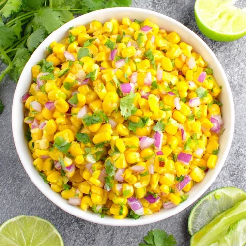 Copycat Chipotle corn salsa in a white bowl with lime wedges and cilantro