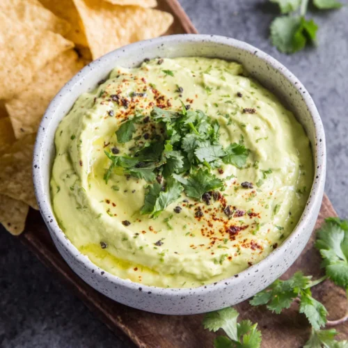 Creamy avocado dip in a bowl with tortilla chips and cilantro garnish