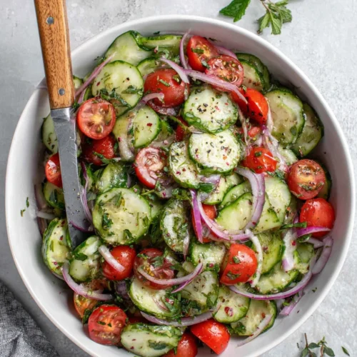 Fresh cucumber tomato salad with red onions and herbs in a white bowl