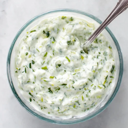 Easy homemade tzatziki sauce in a glass bowl with fresh herbs and cucumber