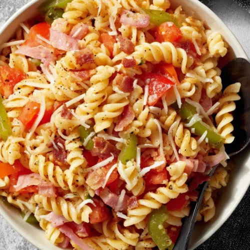 Fourth of July pasta salad with rotini, tomatoes, peppers, and bacon in a white bowl
