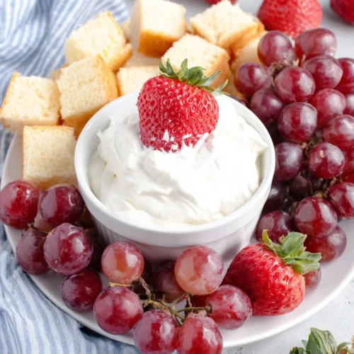 Creamy fruit dip with strawberries, grapes, and pound cake pieces on a white plate.
