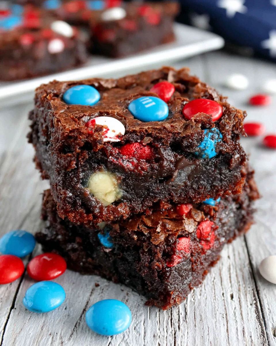 Stacked fudgy brownies with red, white, and blue M&Ms on a rustic wooden surface