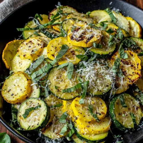 Grilled zucchini and squash slices with parmesan and herbs on a black plate