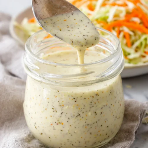 Deliciously Healthy Coleslaw Dressing for Every Occasion 1 Healthy coleslaw dressing in a glass jar with a spoon, creamy texture with visible herbs and spices