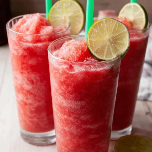 Three glasses of healthy watermelon slushie with lime garnish and green straws