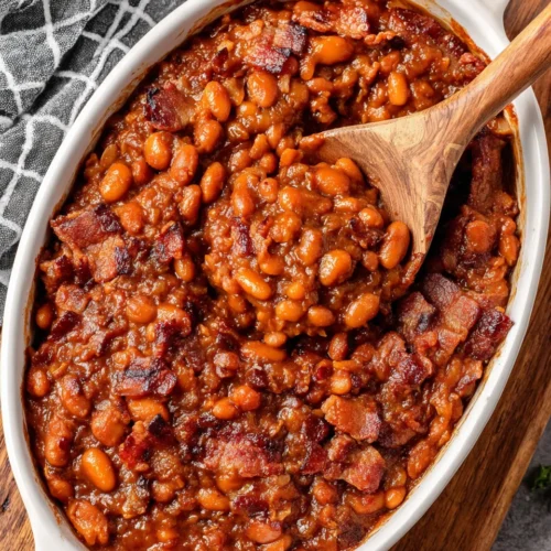 Homemade classic baked beans with bacon in a white dish, wooden spoon