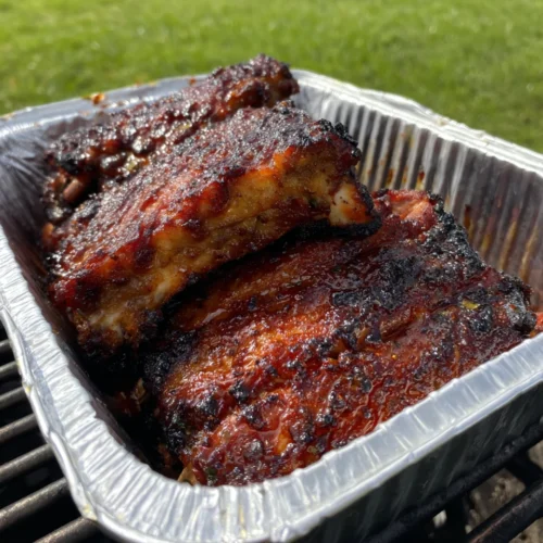 Honey jalapeño party ribs in foil pan, sticky glaze, charred edges