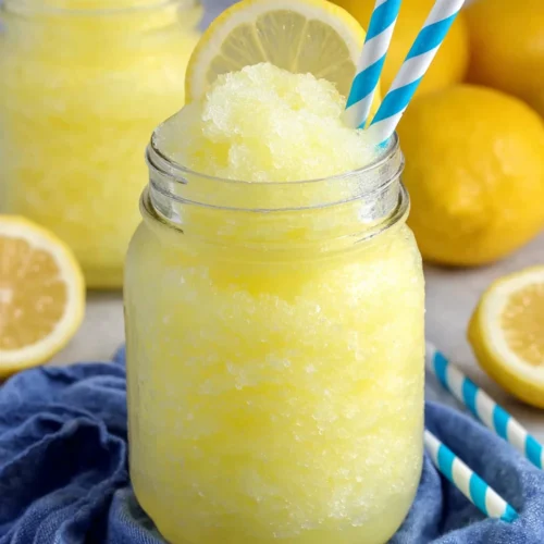 Lemonade slushie in a mason jar with lemon garnish and blue straw