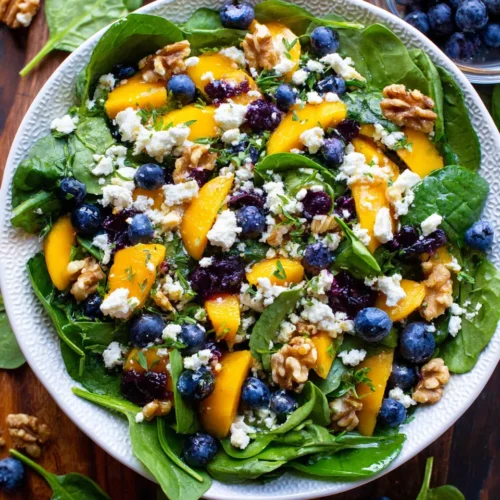 Mango and blueberry salad with spinach, walnuts, and feta cheese on a white plate