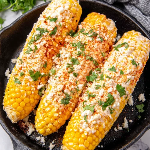 Mexican street corn elote with creamy sauce, cheese, and herbs on a black skillet