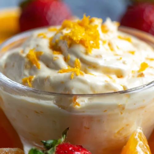 Orange creamsicle fruit dip in a glass bowl with strawberries and orange zest