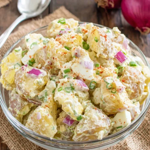 Creamy potato salad with eggs, celery, and red onion in a white bowl