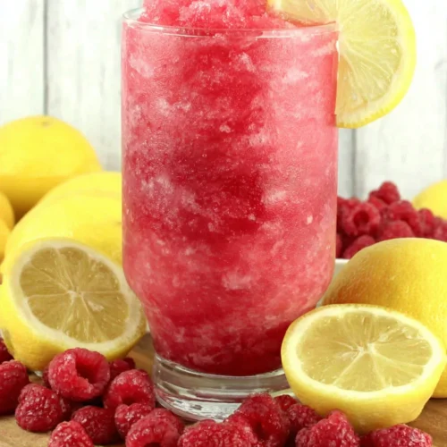Refreshing raspberry lemonade slushie with lemon garnish and fresh berries
