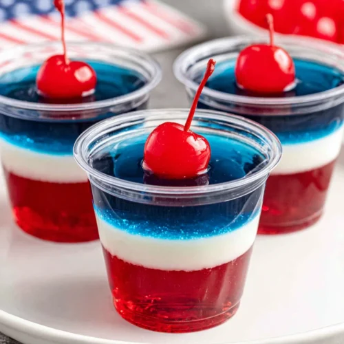 Red white and blue jello cups with maraschino cherries in clear plastic cups