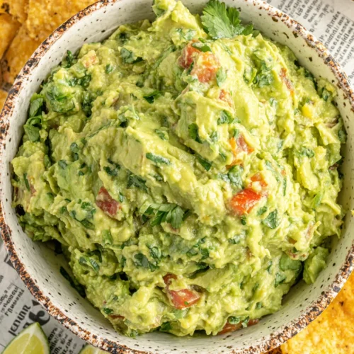 Simple & classic guacamole in a rustic bowl with tomatoes and cilantro