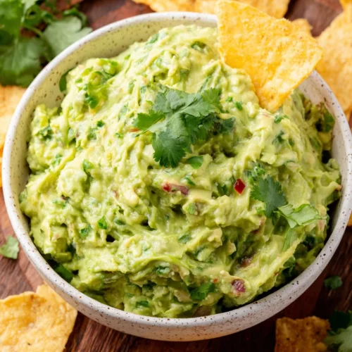 Spicy guacamole in a white bowl with tortilla chips and cilantro garnish