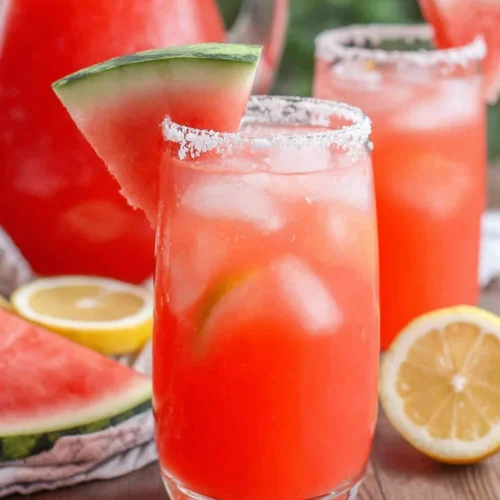 Spiked watermelon lemonade in a glass with ice, salted rim, and watermelon garnish