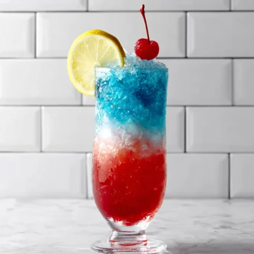 Star-spangled slushie cocktail with red, white, and blue layers, lemon slice, and cherry garnish