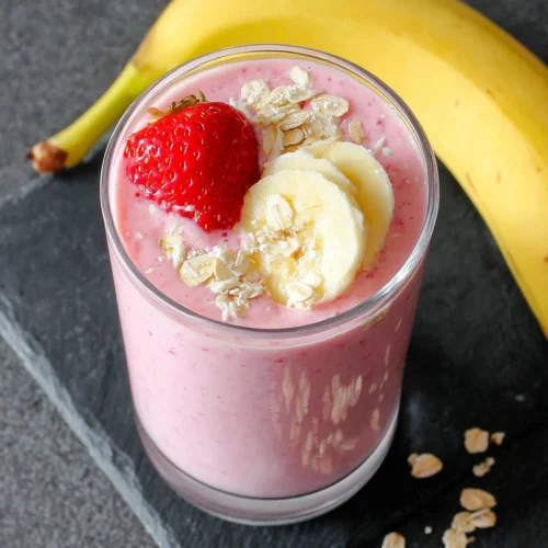 Strawberry banana smoothie with yogurt in a glass, topped with fruit and oats