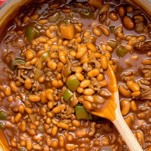 Baked beans with ground beef in a Dutch oven with wooden spoon