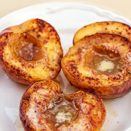 Baked peaches with cinnamon sugar on a white plate, golden and caramelized