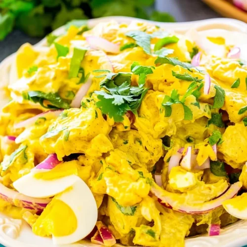 Creamy curried potato salad with eggs, red onion, and cilantro on a white plate