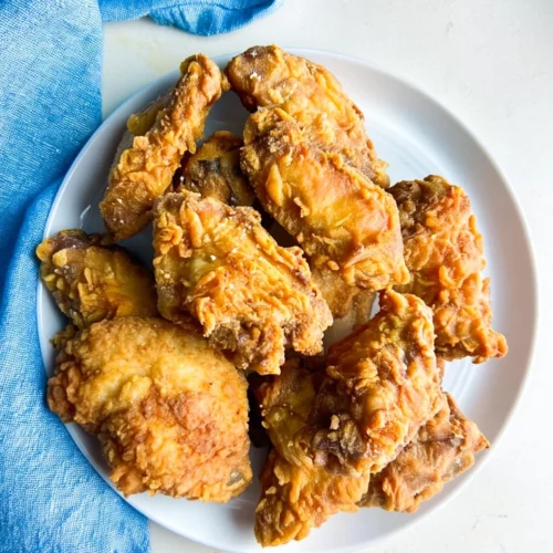 Crispy deep fried chicken wings on a white plate with blue napkin