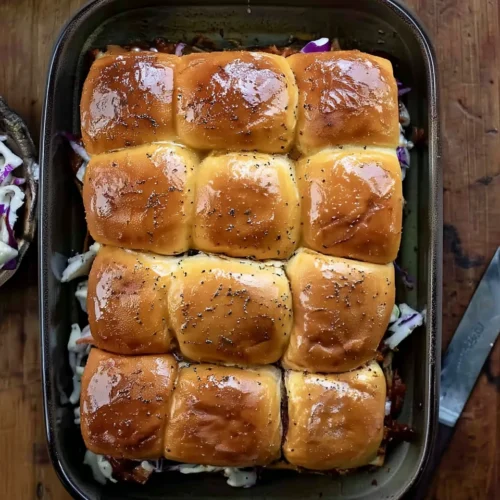 Easy pulled pork sliders in a baking dish with coleslaw and poppy seeds