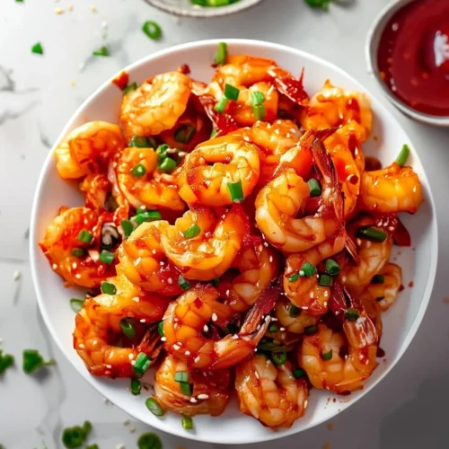 Crispy firecracker shrimp with green onions and sesame seeds in a white bowl